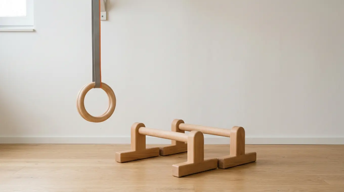 Horizontale minimalistische foto van een paar licht houten parallettes op een lichte vloer, links een set houten ringen met een strap met een dunne oranje streep (#fb8344), zachte